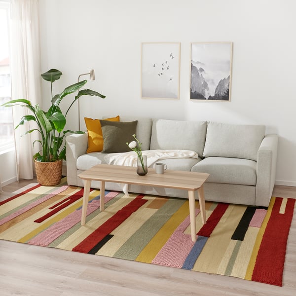 Living room with light grey sofa, wooden coffee table, colourful striped rug, and potted plant. Two framed pictures hang above the sofa.