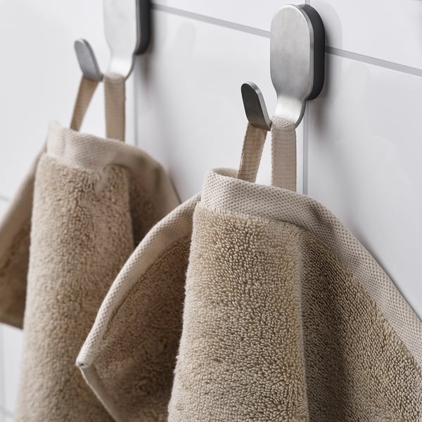 Three beige towels hang on stainless hooks against light wall.