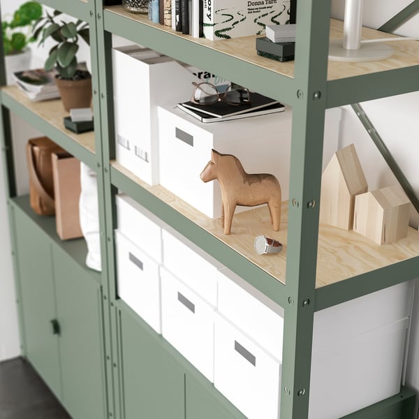Green metal shelving unit with wooden shelves, displaying storage boxes, a wooden horse figurine, plant, and books, suitable for heavy items.