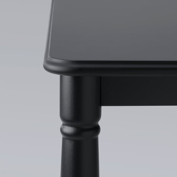 Black table corner with smooth, rounded edges and sturdy, polished legs against a light background.
