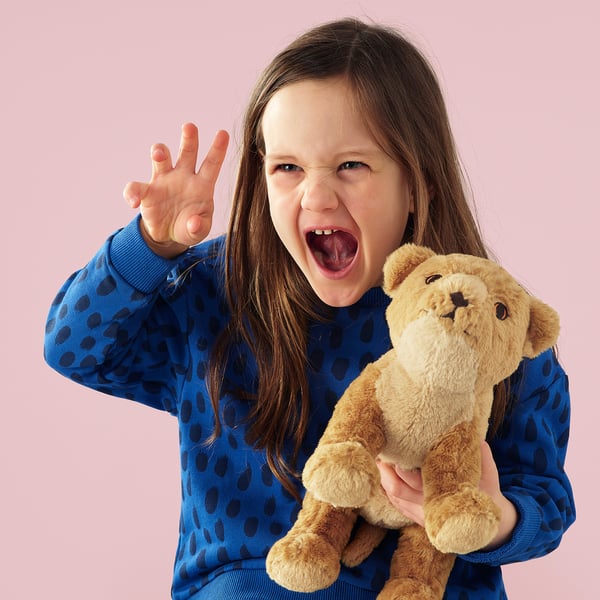 A young girl excitedly holds a soft toy lion, representing a cuddly companion for children.