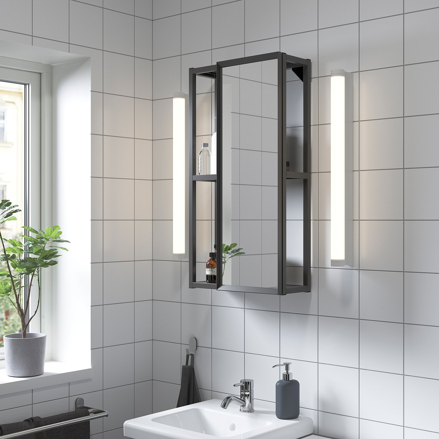 Modern black ENHET bathroom storage cabinet with mirror & lights, smaller than window, holding toiletries, near sink.