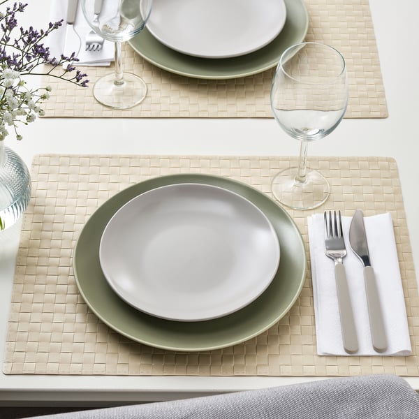 Two place settings with green and white plates, silverware, glass, napkins on woven placemats.