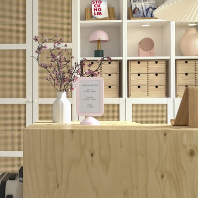 Pink double-sided photo frame, FIKONTRÄD, on wooden desk, surrounded by shelves with books and decor, emphasising its small size.