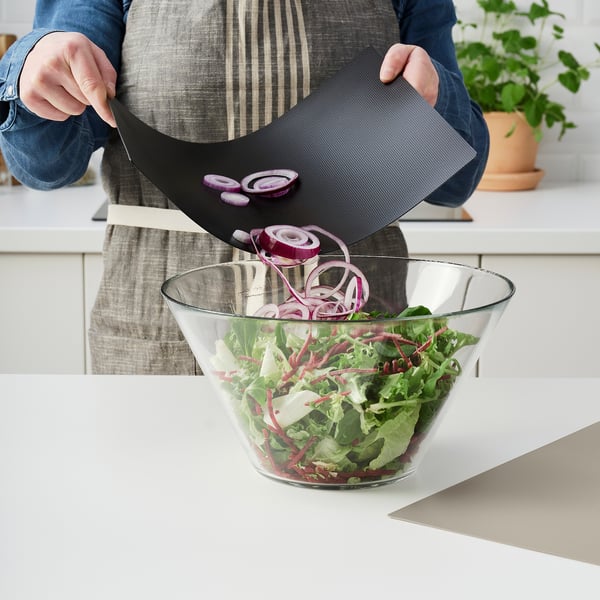 Person uses flexible cutting board to easily slide cut onions into salad bowl. Apron and kitchen setting visible.