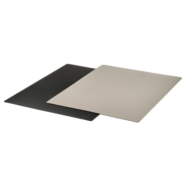 Two FINFÖRDELA flexible cutting boards, black and beige, overlap, designed to protect surfaces and assist sliding chopped food.