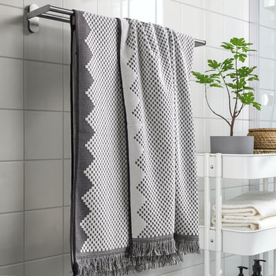Alt: FJÄLLSTARR towel on silver rack, black pattern, grey bathroom with plant.