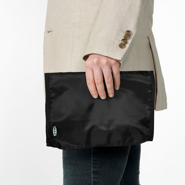 Person holding FODERSKOPA cable organiser, a black, wipe-clean pouch designed to keep cables and small items organised, ideal for travel and home use.