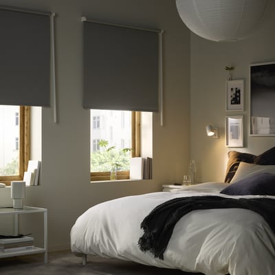 Cosy bedroom with large bed, white linens, dark blanket, plants, nightstands, and pendant lamp