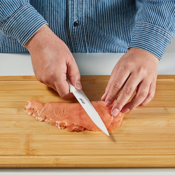 Person slicing food with a ceramic knife on a wooden cutting board.