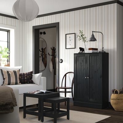 Modern living room with striped walls, featuring a black HAVSTA cabinet, white sofa, black coffee table, wicker chair, and hanging lamp.