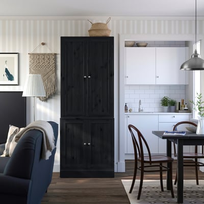 Modern living space with a dark wood HAVSTA cabinet, blue sofa, wooden chairs, and a white kitchen area.