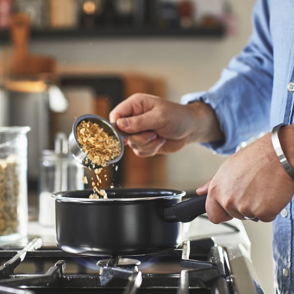 Person pouring food into a non-stick saucepan on a stove. The saucepan has a handle for easy lifting.