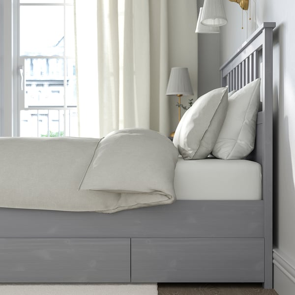 Bed with 4 drawers under for storage, wooden, white neatly made with pillows, lamp beside.