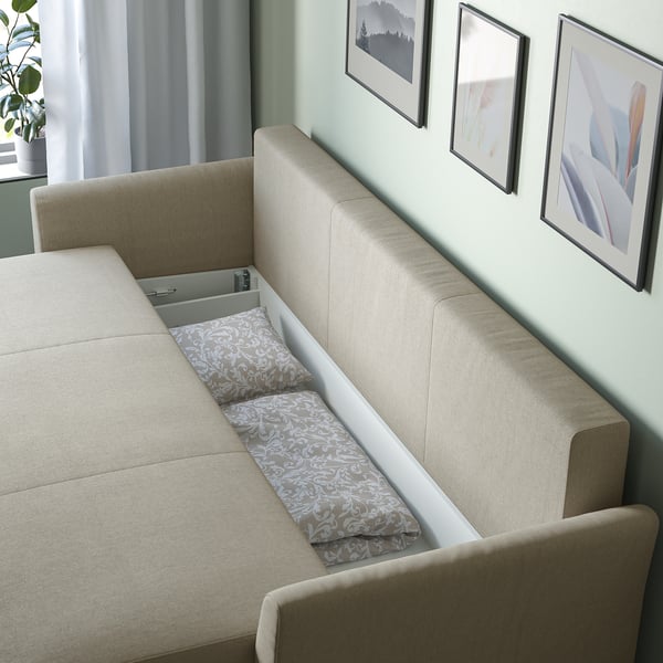 Modern beige sofa with a storage compartment, holding decorative throw pillows. Wall art is visible behind it.