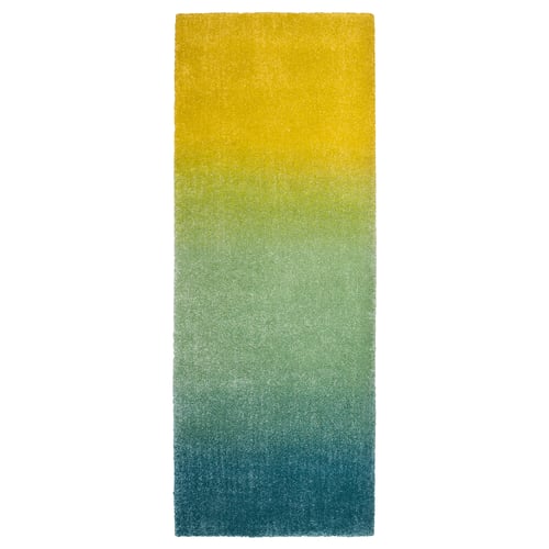 A colourful, rectangular gradient rug in shades of blue, green, and yellow, made of polypropylene, with a soft, inviting texture.