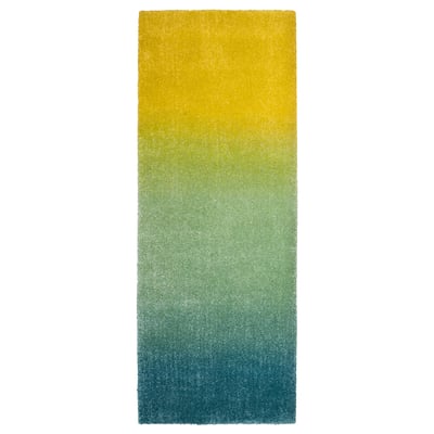 A colourful, rectangular gradient rug in shades of blue, green, and yellow, made of polypropylene, with a soft, inviting texture.