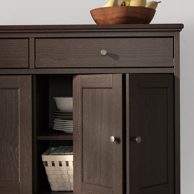Dark brown wooden sideboard with bi-folding doors and a drawer, displaying white plates and a woven basket.