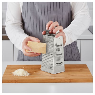 Person grates cheese using a dual-sided stainless steel grater on a wooden cutting board.