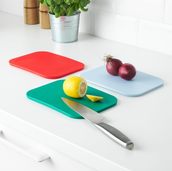 Three colourful cutting boards on a white countertop: red, blue, and green. One has onions, another has a lemon and knife.