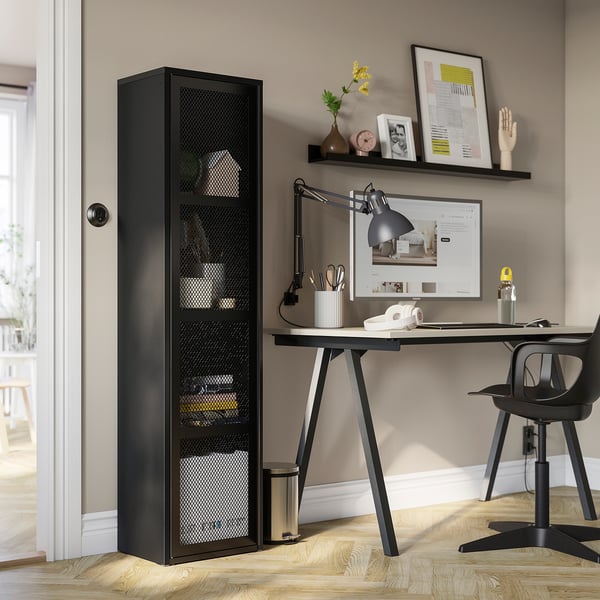 Black IVAR cabinet with mesh next to wooden desk and computer. Fits well, larger than office chair.