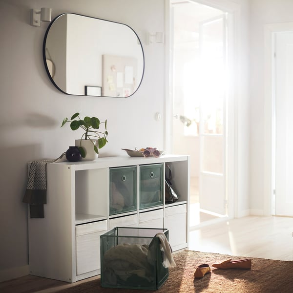 White KALLAX cubed storage cabinet with mirrored wall decor, room lit by sunlight.