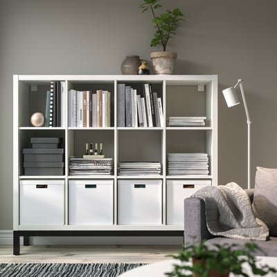 The KALLAX white shelf holds books and decor. Its large size fits many items, prominently displayed against a wall.