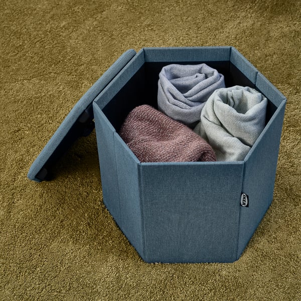 Hexagon storage bin holding folded blankets on beige carpet.