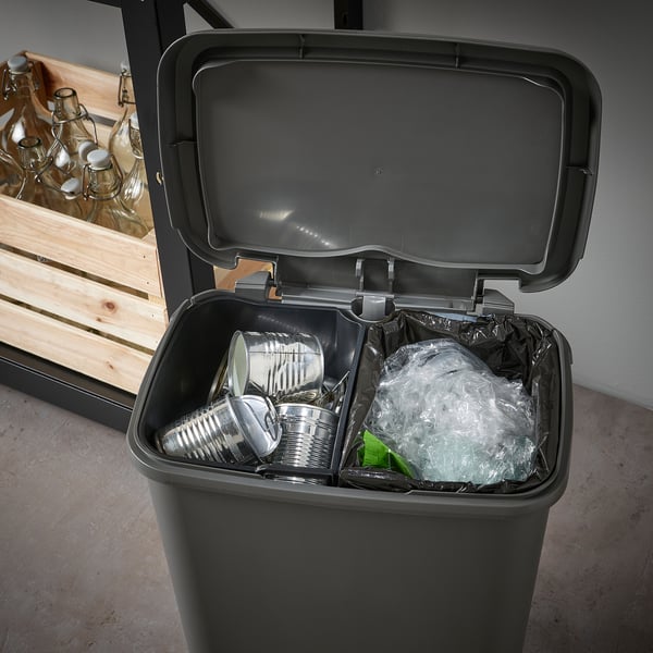 Black pedal bin with two inner compartments, one with cans and the other with plastic waste, designed for waste separation.