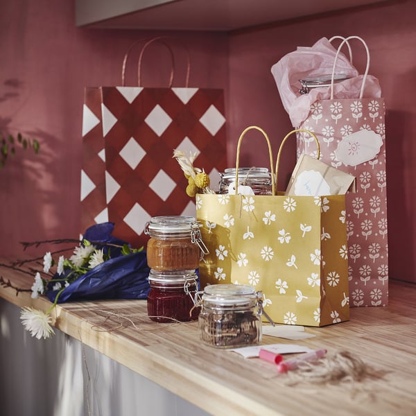 KÖSSEBÄR gift bags in yellow & red with white floral designs. Different sizes; largest holds jars, smallest fits small items. Made of recycled paper.
