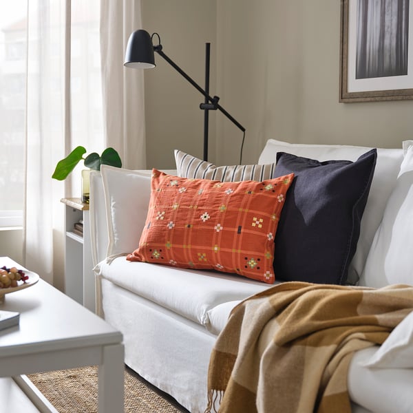 Bright living room with KUSTGRAN orange cushions on a white sofa. Black floor lamp beside, beige curtain in the background.