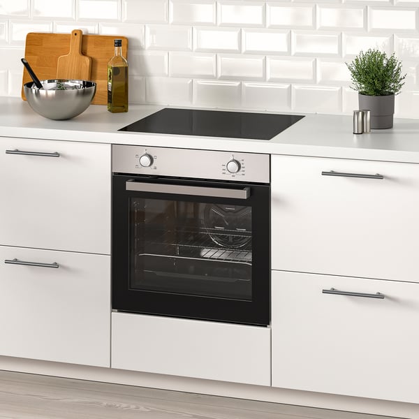 Modern kitchen with white cabinets, a built-in oven, and a countertop featuring a plant, cutting board, bowl, and oil bottle.