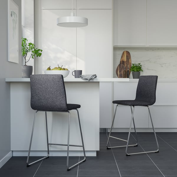 Minimalist kitchen with grey barstools and white countertop, holding fruit, mug, and plants.
