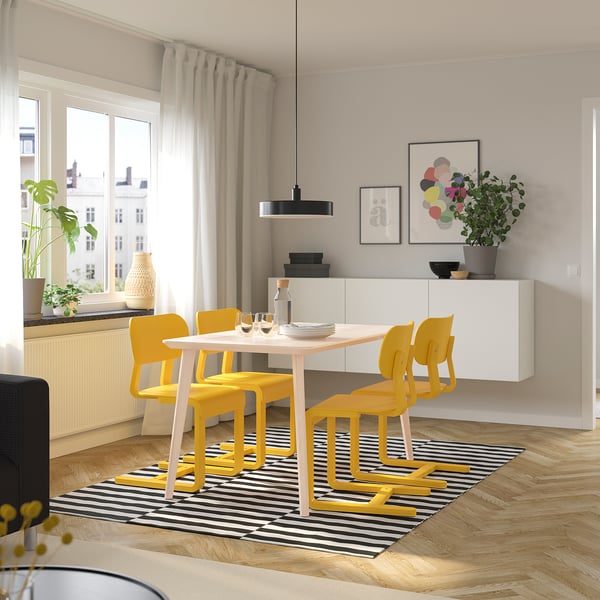 Bright dining set with yellow chairs, modern design, positioned under a large window, complementing the white table and wall decorations.