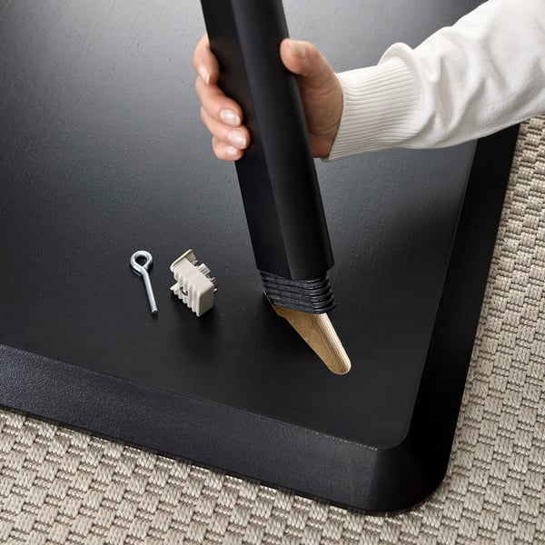 A person assembles a LISABO table by attaching legs with a single fitting. The table has a sleek, modern black finish and sturdy wood construction.