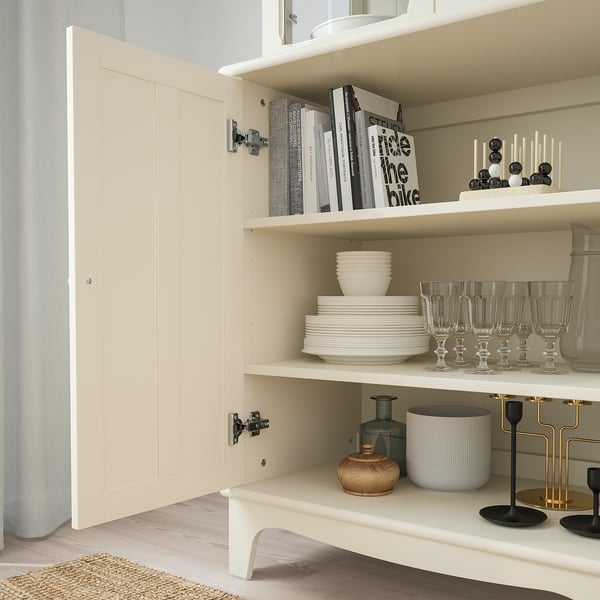 Open cream cabinet displaying plates, glasses, books, and decorative items. Adjustable shelves visible, soft-close hinges evident.