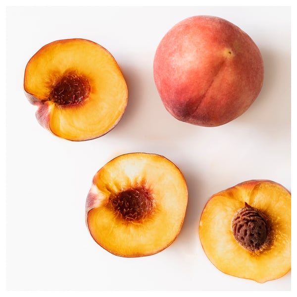 Top view of four peaches: whole and halved, bright red skin, yellow flesh, arranged on white.