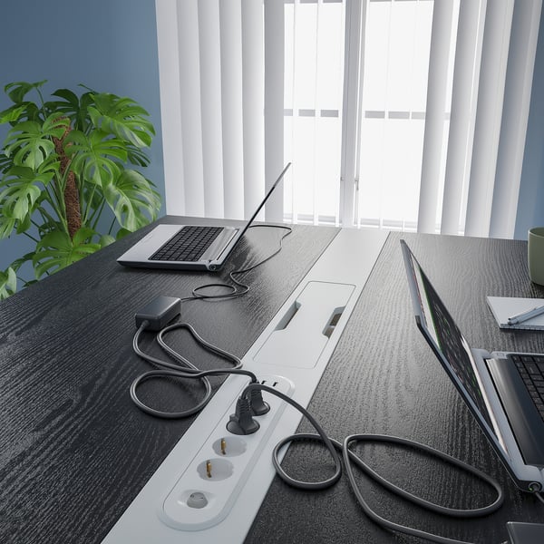 Office table with multiple laptops, cables, and power strips for tech support. A potted plant adds decor.