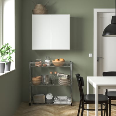 Modern green kitchen with white cabinet, OLAUS rack, plant, and black chair.