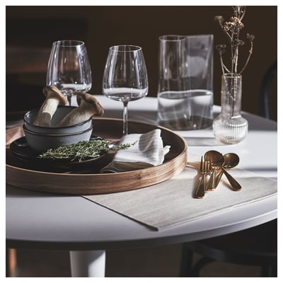 Dark wood round serving tray with grey bowl, mushrooms, herbs, golden utensils, wine glasses, vase, white linen on table.