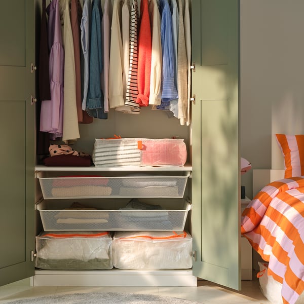 Open closet showing clothes hung neatly on top, middle shelf with colourful folded linens, and bottom with white organiser bins holding stored items.