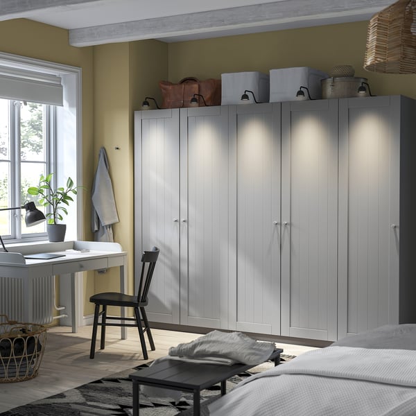 PAX wardrobes, grey, wooden, freestanding, shelves & rail. Topped with boxes, bags, lantern. Desk with chair, window, plant basket.