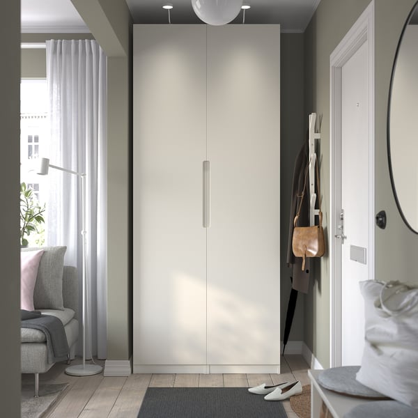 Modern white PAX wardrobe beside entry door, taller than adjacent shoe rack.