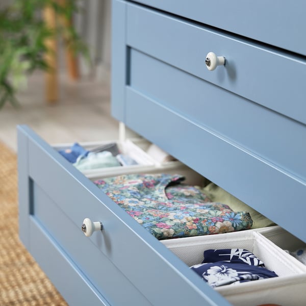 Light blue PLATSA drawer unit with organised clothes; floral dress & folded scarves in compartments.