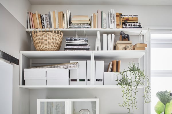 White PLATSA shelving unit with books, basket, boxes, and plants. Neatly organised, minimalistic design.