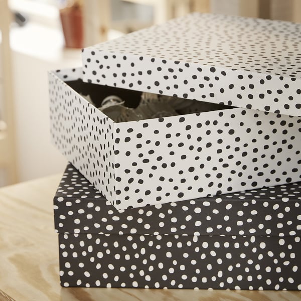 Two polka-dotted storage boxes stacked, top one open showing items inside, on wooden surface.