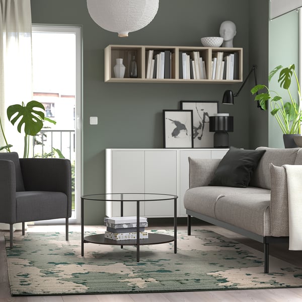 Modern living room with RINGKLOCKA patterned rug, grey sofa, plants, green walls, natural light.