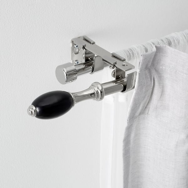 Modern curtain rod hardware featuring polished metal and black accents, securely holding a white curtain, showcasing sleek and sophisticated design.