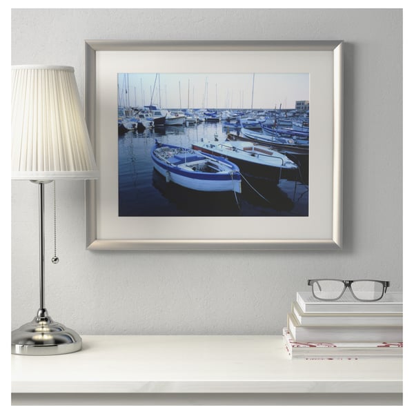 A modern desk setup with a framed boat photo, a lamp, and books.