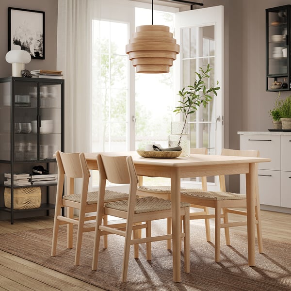 Minimalist dining set with light wooden table and matching chairs, accented by a pendant lamp and potted plant on a wooden floor.